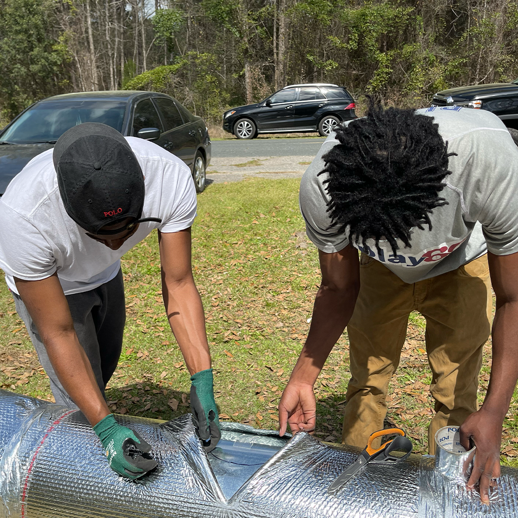 Two students in the field training on HVAC duct